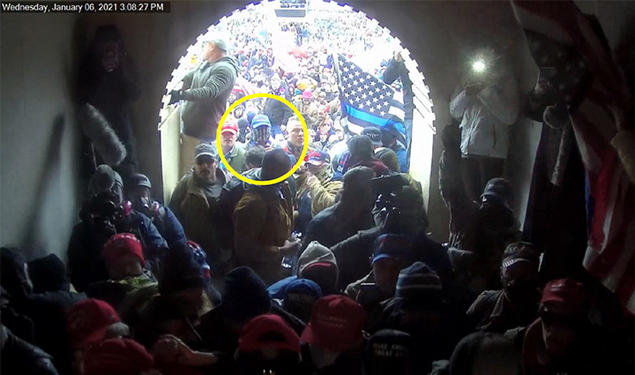 The view out of a crowded Capitol entrance tunnel; a yellow circle highlights Giberson facing the entrance wearing a blue baseball cap and a gaiter over his face.