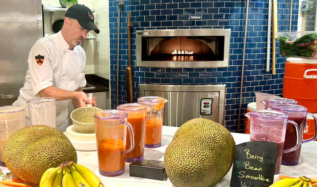 Dining staff prepare vegan berry bean smoothies on a table with bananas and jackfruit.