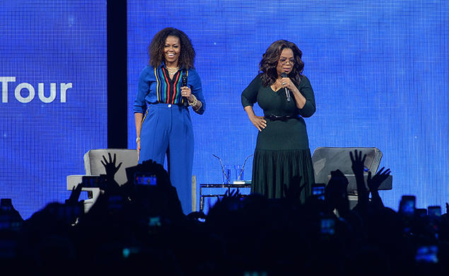 Michelle Obama and Oprah address an audience from a stage.