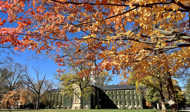 The back of Nassau Hall with tree branches with fall leaves in the foreground.