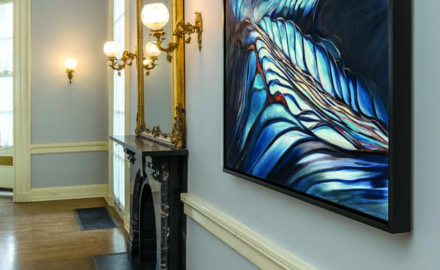 This is a photo "Pools," an abstract painting with lots of blue, hanging in Prospect House on a gray wall with a chair rail and crown moulding, next to a fireplace with a gilded mirror over it.