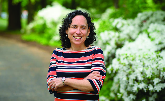 This is a photo of Rabbi Julie Roth outdoors, with green shrubs in the background.