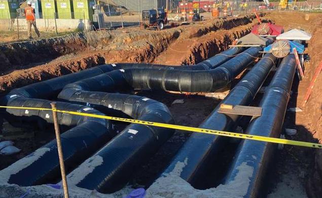 This is a photo of the thermal piping installed near Jadwin Gym — four big black pipes down in a dug-out area of reddish dirt..