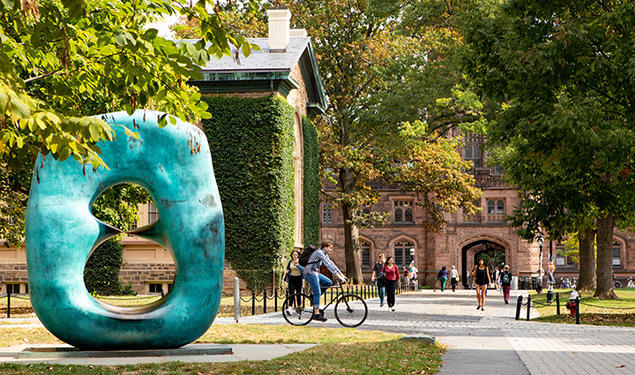 This is a photo of the Oval With Points sculpture with East Pyne and lots of students in the background.