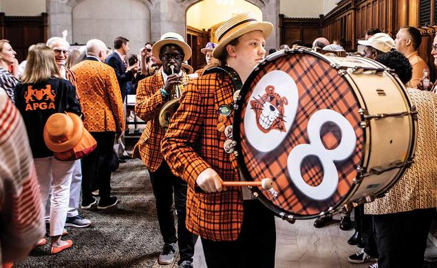 This is a photo of a few Princeton musicians wearing plaid blazers and straw hats while marching. The one in front has "08" printed on his drum.