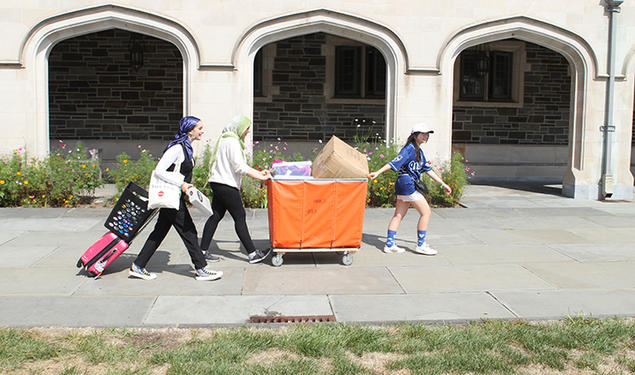 Three women push and pull a large orange bin.