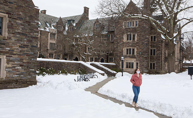 A masked student walks across campus, on a path cut through the snow, in 2021.