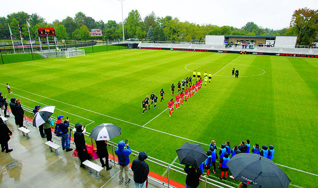 Women’s soccer players walk onto the field in two lines before the start of the game.