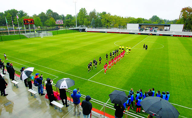 Women’s soccer players walk onto the field in two lines before the start of the game.
