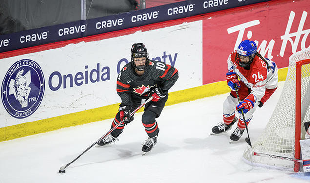 Two hockey players skate around the back of the goal.