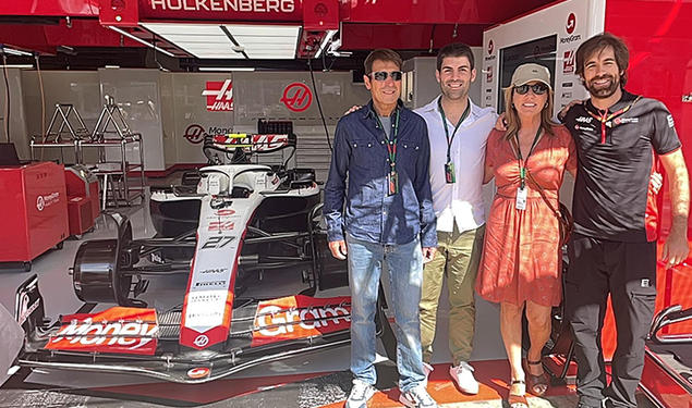 Stefano Chiazza *13 and three other people stand in a garage with a Formula 1 racecar.