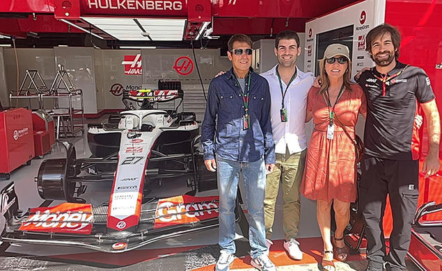 Stefano Chiazza *13 and three other people stand in a garage with a Formula 1 racecar.