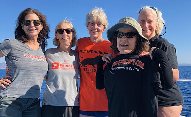 Five women standing on a boat wear various Princeton T-shirts.