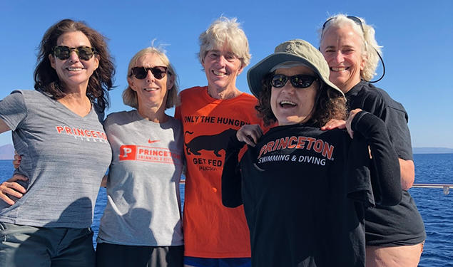 Five women standing on a boat wear various Princeton T-shirts.