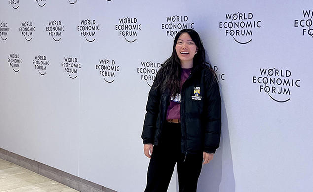 Diana Chao stands in front of a wall printed with the logo for this year's World Economic Forum.