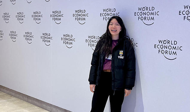 Diana Chao stands in front of a wall printed with the logo for this year's World Economic Forum.