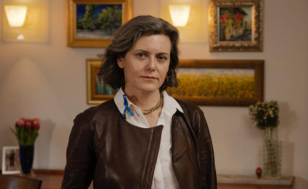 This is a photo of Dora Chomiak ’91 in front of a wall hung with paintings.