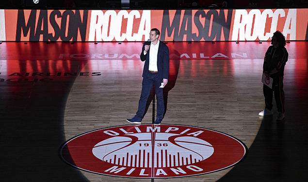 Mason Rocca ’00 stands in a spotlight on a basketball court that reads "Olimpia Milano."