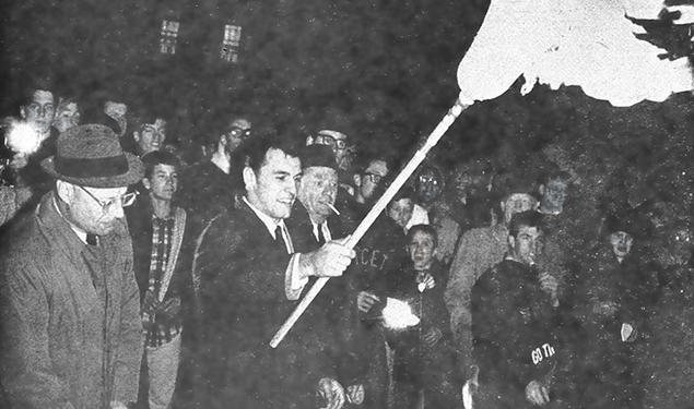 All-American Cosmo Iacavazzi ’65 *68 lights the bonfire, with coach Dick Colman (in glasses) by his side.