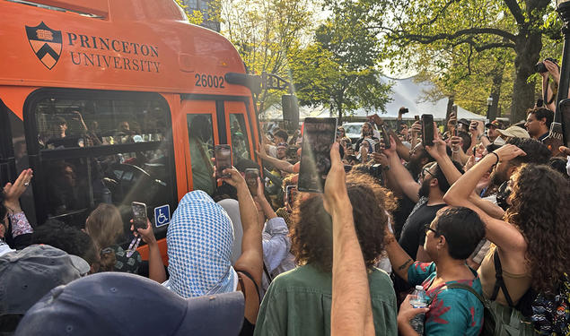 Protesters surrounding a University bus, holding up cell phone cameras