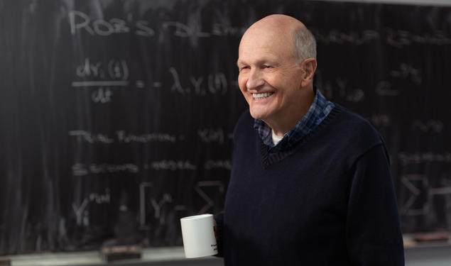 This is a photo of Frank N. von Hippel in front of a chalkboard. He's holding a coffee mug.