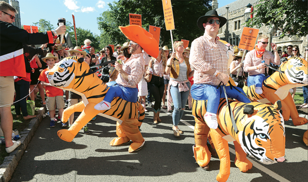 This is a photo from the P-rade in 2017 of the Class of 2002 riding inflatable tigers. One is wearing an orange cowboy hat.