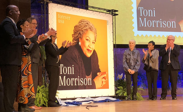 Seven people stand next to a large poster of a postage stamp featuring Toni Morrison