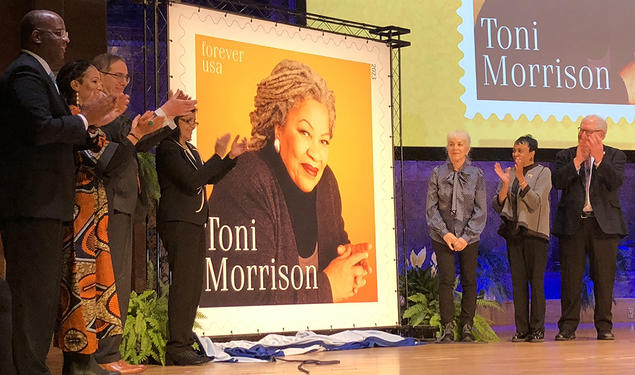 Seven people stand next to a large poster of a postage stamp featuring Toni Morrison