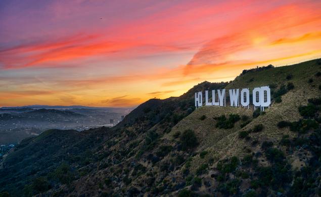 The sun sets behind the famous HOLLYWOOD sign on a hill in California.