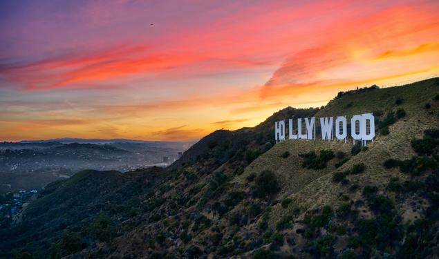 The sun sets behind the famous HOLLYWOOD sign on a hill in California.