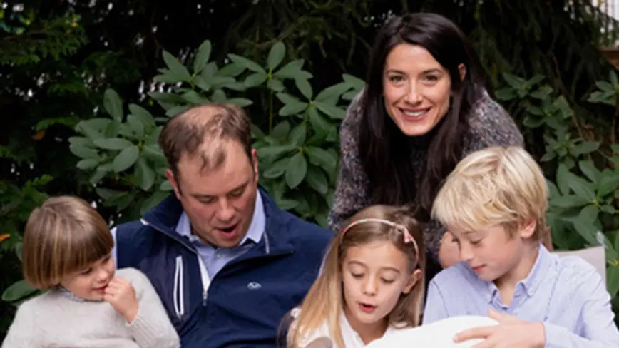 Podcaster Milano Buckley ’02 on Parenting and an Unusual Childhood Milano Buckley looks up and smiles in a family photo where her husband and three children are all looking down.