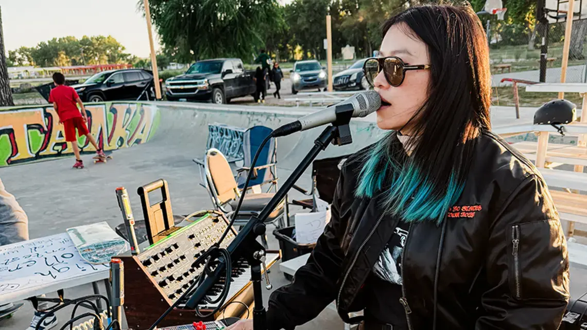 A woman sings into a microphone in a skate park.