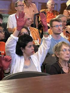 A woman in the audience holds up her hands wearing red surgical gloves.