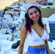 Anika Asthana ’25 smiles with quaint white and blue homes on a Greek island in the background.