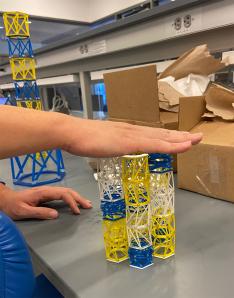 Someone holds their hand over a set of small blue, yellow, and white structures that look like scaffolding.