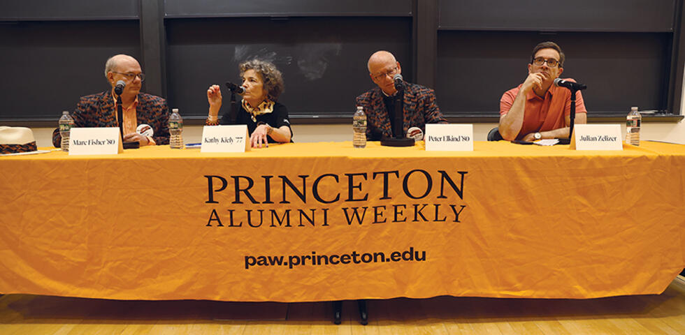 Four people sit at a long tabble draped with an orange cloth. 