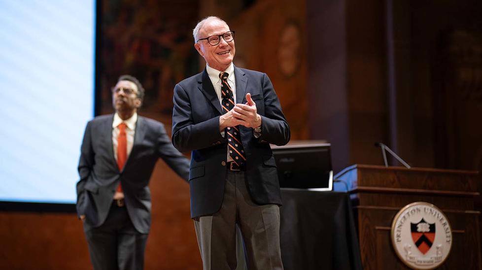 David Card on stage with Graduate School dean Rodney Priestley in the background