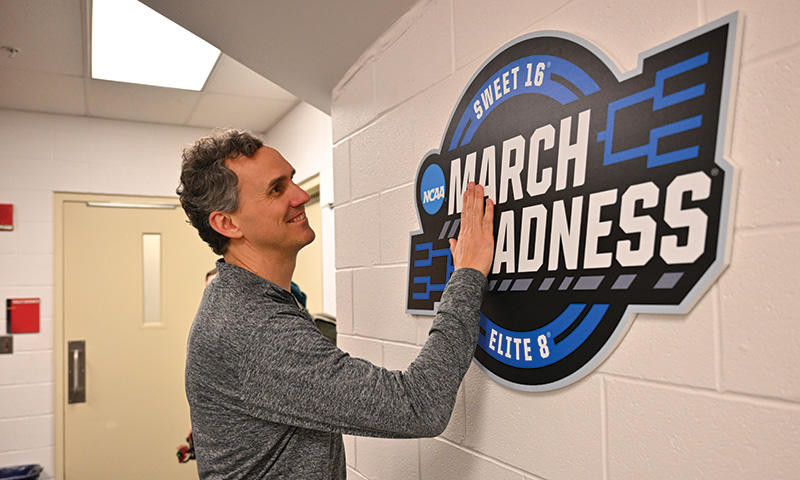 Head coach Mitch Henderson ’98, center, touching March Madness signage