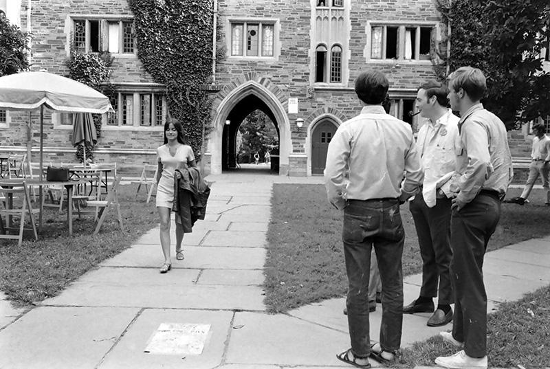 An undergraduate woman walking past three male students