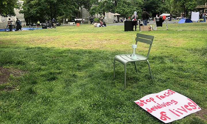 An empty chair on Cannon Green and a sign on the ground that reads, "Stop racist devaluing of lives!"