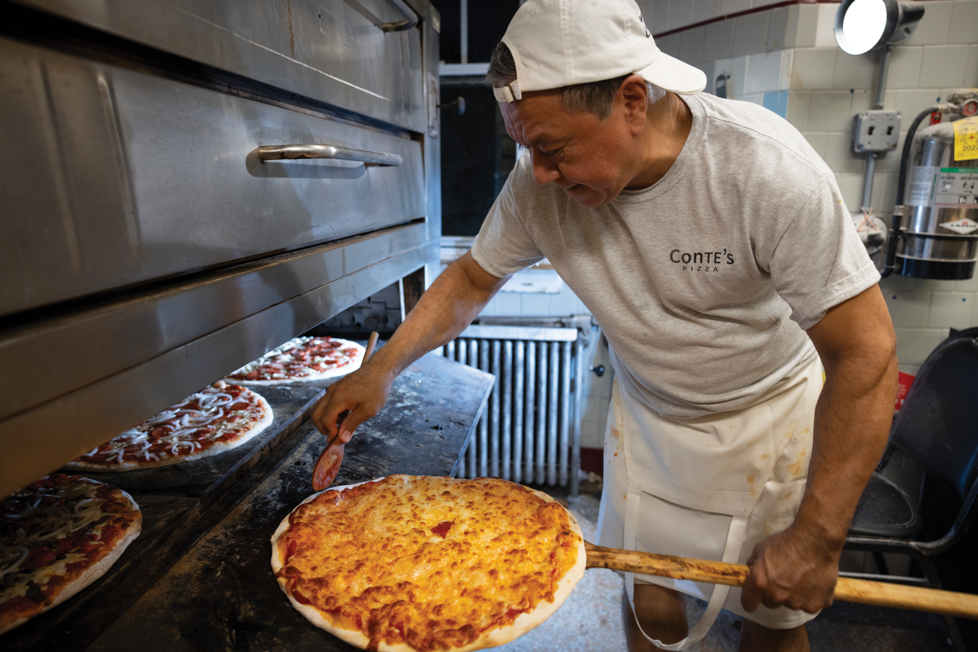 A cook at Conte's pulls a pizza out of the oven.