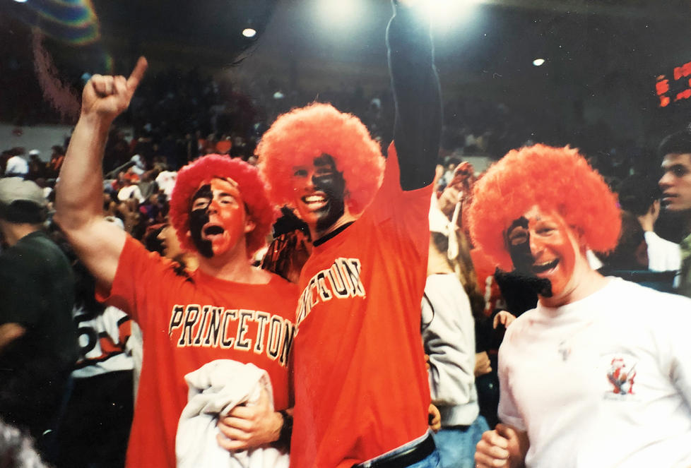 Wearing a puffy orange wig and orange-and-black face paint, Grant Wahl ’96, center, cheers for Princeton at a men’s basketball game.