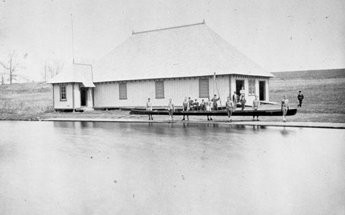 Crew members prepare for practice in front of the original campus boathouse in 1875