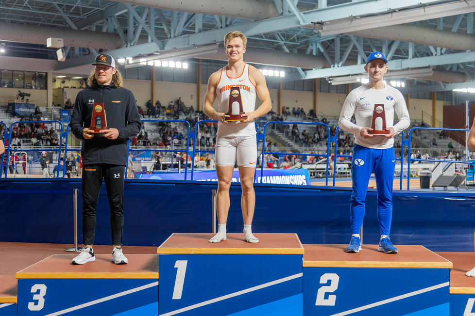 This is a photo of three pole vaulters holding trophies on the podium; Sondre Guttormsen ’23 stands highest in the center.