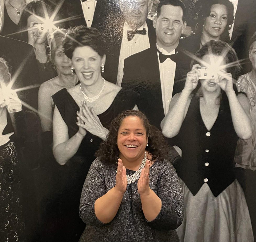 Janice Johnston claps her hands in front of a black-and-white poster of a cheering crowd.