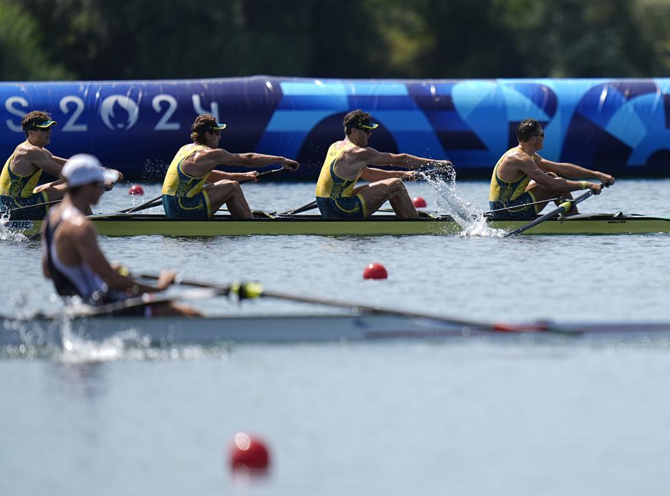 Four rowers competing in the Olympics, one rower from another boat is visible in the foreground