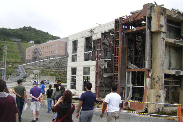 Students walk past a three-story concrete building in Onagawa tipped by the tsunami, whose waters reached the red-brick hospital at left.